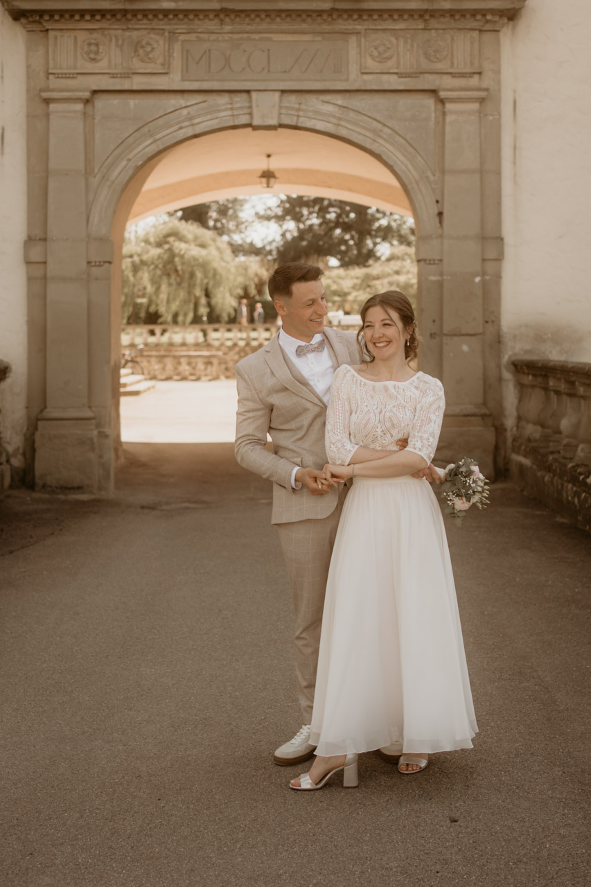 Christian Messner fotografiert lachendes Brautpaar beim Hochzeitsshooting vor dem Schlossbogen