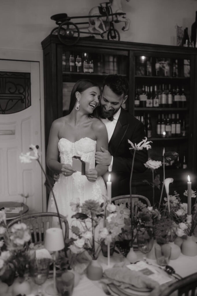 Zärtlicher Moment zwischen Braut und Bräutigam, die sich lachend umarmen – umgeben von Kerzenlicht und floraler Dekoration.