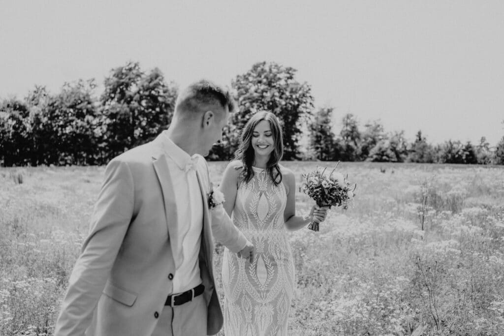 Schwarzweißaufnahme eines verliebten Brautpaars beim Spaziergang durch ein Blumenfeld – fotografiert von Christian Messner