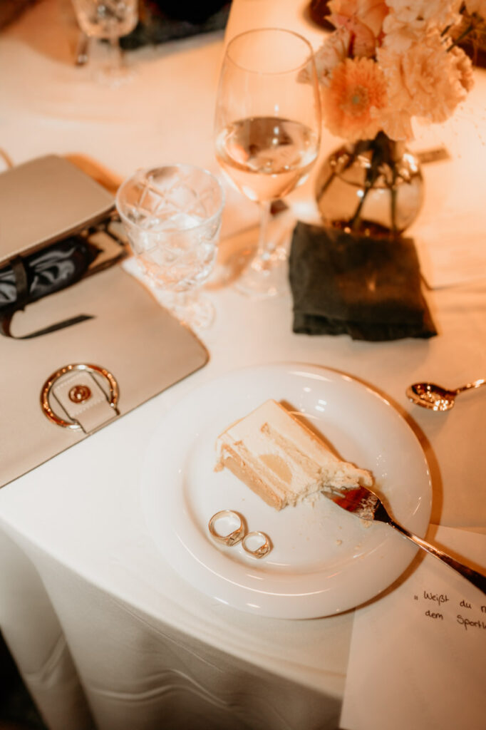 Detailaufnahme mit einem Stück Hochzeitstorte und zwei Eheringen auf dem Teller – festgehalten vom Hochzeitsfotograf als leiser Moment voller Bedeutung