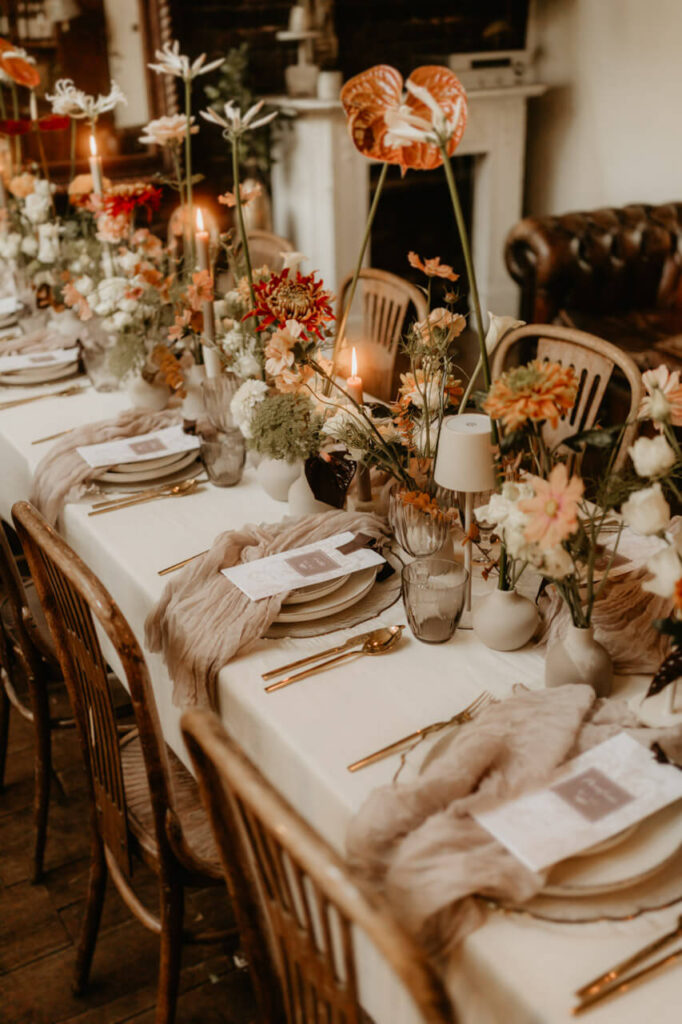 Eleganter Hochzeitstisch mit feiner Tischdekoration, goldfarbenem Besteck, Kerzenlicht und zarten Blumenarrangements in warmen Tönen.