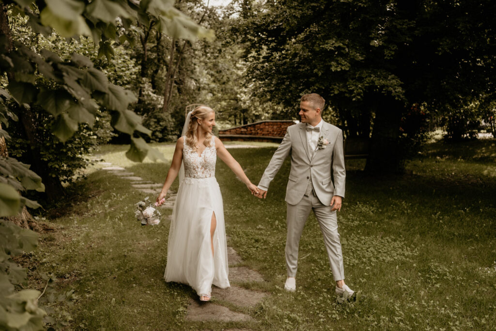 Braut und Bräutigam Hand in Hand im Grünen – eingefangen von Hochzeitsfotograf Christian Messner.