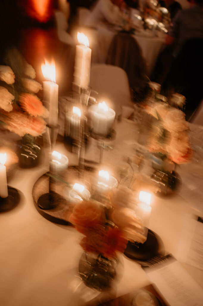 Kerzenschein und verschwommene Blüten auf einem Hochzeitstisch – ein stimmungsvolles Detailbild von Christian Messner