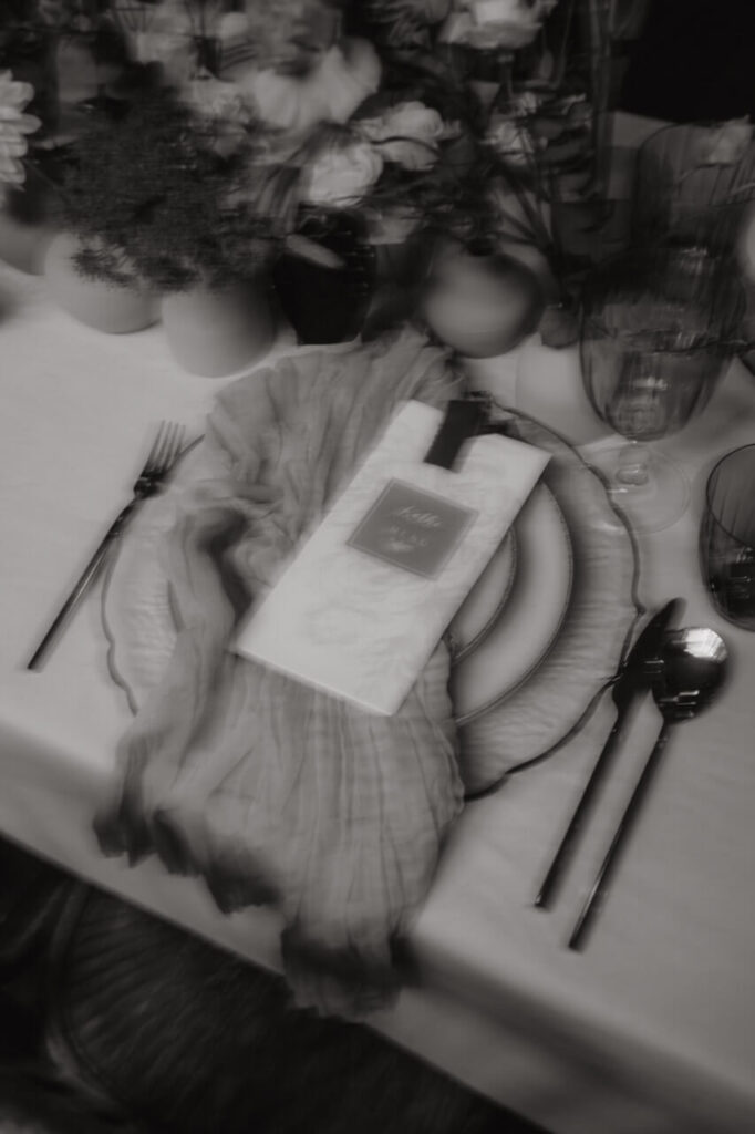 Christian Messner fotografiert ein elegant arrangiertes Hochzeitstisch-Detail mit Menükarte, Glasgeschirr und floralen Akzenten in sanftem Licht.