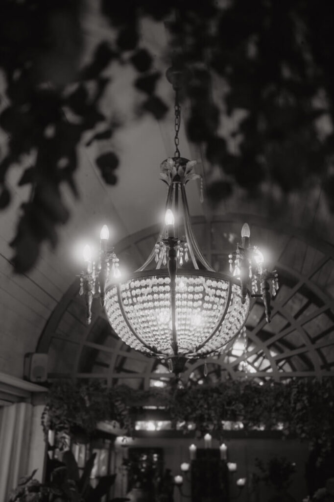 Der Hochzeitsfotograf fängt einen stimmungsvollen Kronleuchter mit warmem Licht und floraler Dekoration in einer romantischen Hochzeitslocation ein.