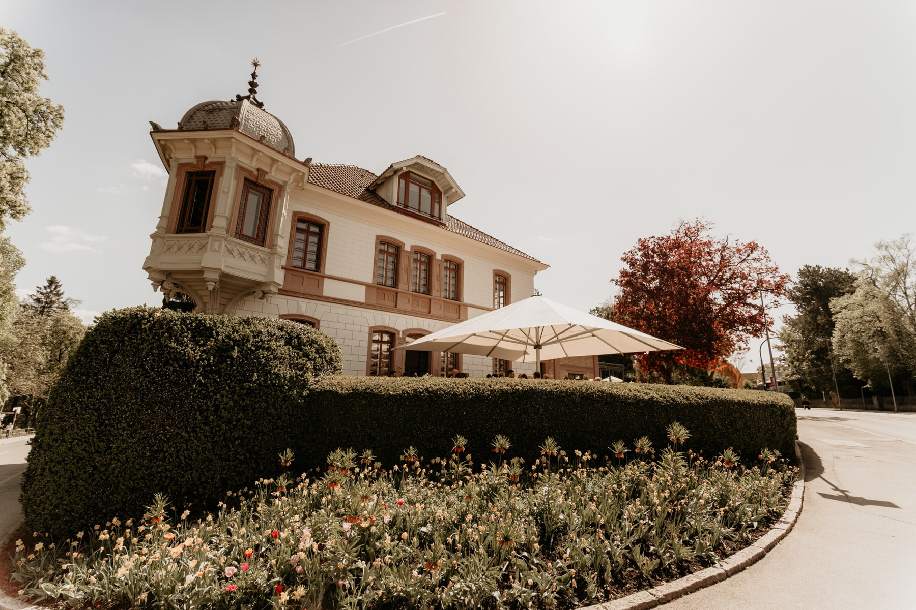 Historische Villa mit Türmchen, gepflegtem Vorgarten und weißem Sonnenschirm bei Sonnenschein